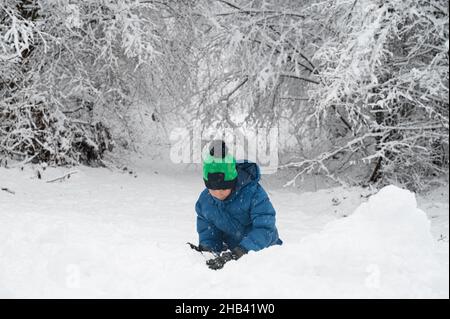 Garçon en costume d'hiver jouant dans la neige dehors dans une belle nature enneigée d'hiver. Banque D'Images