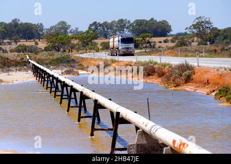 Conduite d'eau de fond sur des peuplements traversant le lac salé avec un camion de passage, Wongan Hills, Australie occidentale Banque D'Images