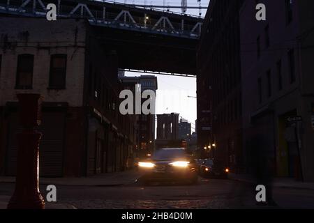 Rue sombre de Brooklyn la nuit sous les ponts de Manhattan et de Brooklyn avec phares et silhouettes.Arrière-plan à exposition longue avec aspect rétro. Banque D'Images