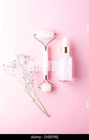 Composition d'une bouteille de sérum mockup, rouleau frontal en pierre de quartz rose avec fleurs de gipsophyla sur fond rose.Concept de cosmétiques naturels.Cosme créatif Banque D'Images