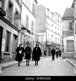 Paris Monmartre - piétons rue Norvins, hiver 1945.Le photographe se tient devant le 3 rue Norvins pour enregistrer les piétons dans un cadre intime.Seuls huit secoueurs sont en vue.Le groupe clé est une jeune femme qui marche avec deux femmes d'âge moyen à ses côtés.Deux des trois yeux le photographe; la jeune femme semble alarmée.Les vêtements indiquent que c'est une journée froide. Banque D'Images