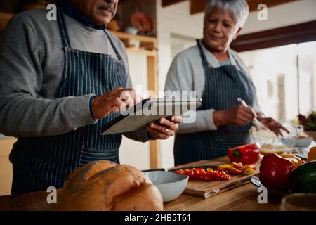 Couple de personnes âgées multiculturelles utilisant une tablette pour rechercher une recette dans la cuisine.Heureusement à la retraite de la cuisine repas sain. Banque D'Images