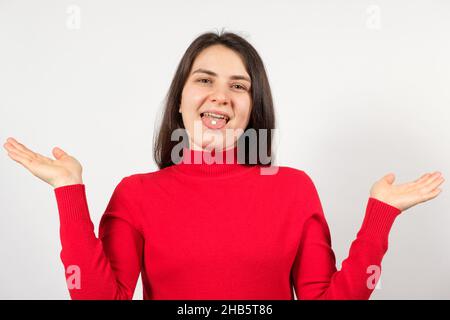 Une femme avec des pilules sur sa langue se répand ses bras sur un fond blanc. Banque D'Images