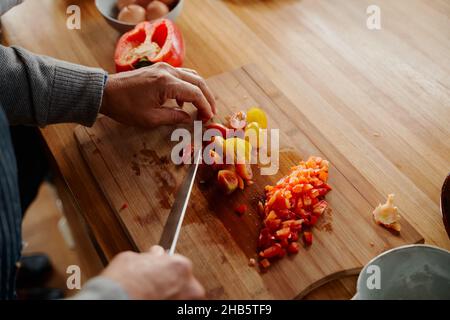 Les mains de femmes âgées multiculturelles hacher des légumes colorés sur une planche à découper en bois.Un petit déjeuner sain à la maison, à la retraite. Banque D'Images