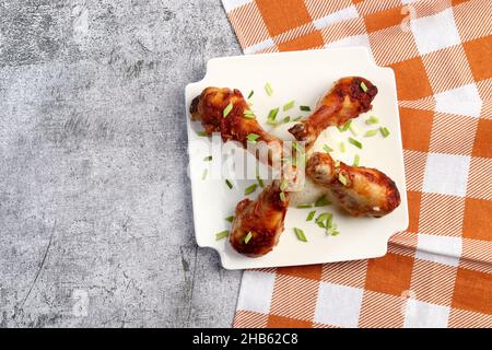 Pilons de poulet cuits au four avec du riz sur une assiette carrée blanche sur fond sombre.Vue de dessus, plan d'appartement Banque D'Images