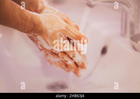 Un homme lave soigneusement ses mains avec du savon suds sur un évier en céramique blanche dans la baignoire.Propreté et hygiène. Banque D'Images