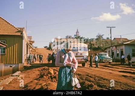 Arrêt de bus dans un village rural sur la route entre Curitiba et Foz do Iguaçu, Laranjeiras do sol, État de Paraná, Brésil en 1962, la femme touriste passager au premier plan Banque D'Images