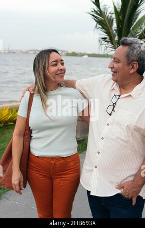 Couple hispanique d'âge moyen souriant et embrassant au parc Banque D'Images