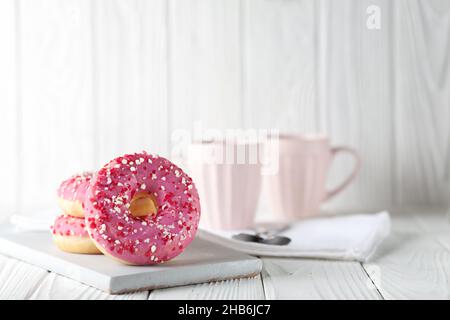 Beignets à la glaçure rose et à la poudre de caramel colorée sur fond blanc en bois. Banque D'Images