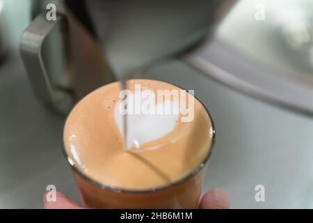 Le barista prépare un dessin avec du lait en forme de cœur dans un verre de cappuccino. Banque D'Images