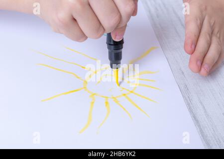 Les mains des enfants dessinant avec un stylo feutre, un stylo un soleil jaune heureux sur le papier.La création artistique à la maison, fait des œuvres d'art créatives.Divertissement à la maison goélette Banque D'Images