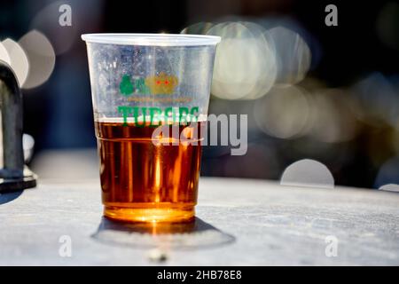 Tuborg, bière dans un verre en plastique avec des empreintes visibles des doigts, à moitié plein Banque D'Images