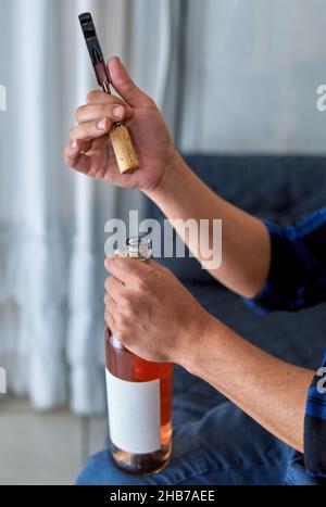 mains de latins qui décornèrent une bouteille de vin de rose tout en étant assis sur un canapé à la maison.Verticale Banque D'Images