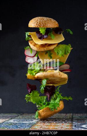 Tranches de hamburger à lever.Nourriture volante.Pain hamburger, double escalope de poulet avec fromage, laitue, arugula et radis.Viande, légumes et pain.Ingrédients sur fond noir. Banque D'Images