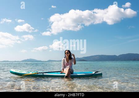 Portrait d'une femme heureuse avec des lunettes de soleil assis à bord inférieur dans l'océan. Banque D'Images