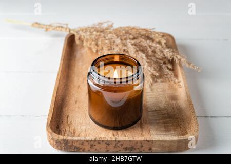 Bougie parfumée dans un pot en verre maquette sur un plateau en marbre et plante d'herbe sèche sur fond de bois blanc Banque D'Images