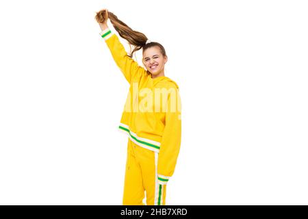 Photo de beau drôle heureux merveilleux sourire mignonne fille avec cheveux foncés avec queue de cheval dans élégant jaune tracksuit avec des rayures vertes isolées dessus Banque D'Images