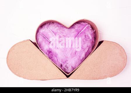 Plumes violettes lilas dans une boîte cadeau en forme de coeur sur fond blanc. Banque D'Images