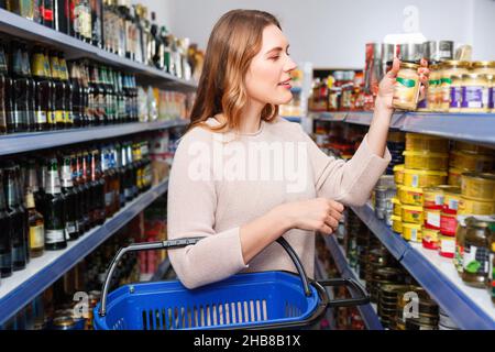 Cliente positive avec un panier contenant des conserves dans le magasin de produits alimentaires Banque D'Images