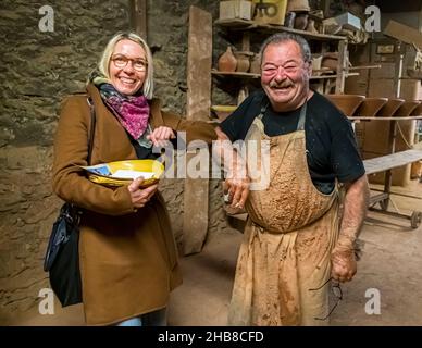 Le propriétaire de Poterie Not Frères partage un rire avec la journaliste Angela Berg dans l’atelier près de Mas-Saintes-Puelles. La cassole est le moule en terre cuite dans lequel le cassoulet est préparé. L’atelier sur le Canal du Midi, dans le département de l’Aude, en France, a été fondé au début du XIXe siècle par la famille Perrutel et est géré par la famille Not depuis 1947, connue pour ses cassoles fabriquées à la main, le plat traditionnel du cassoulet. Banque D'Images