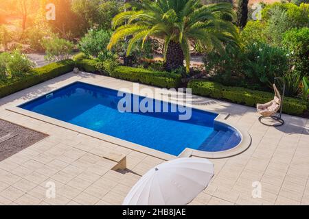 Une piscine moderne dans le jardin avec des palmiers pour la détente des touristes près de l'hôtel.Vue de dessus, été, fauteuil à bascule. Banque D'Images