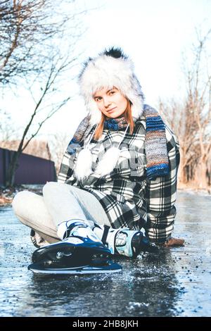 La fille est assise sur la glace.Fille patinage sur glace.Patinage artistique.Loisirs d'hiver.Glaçage hivernal de l'asphalte Banque D'Images