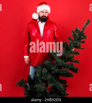 Homme barbu en veste rouge et chapeau de père Noël avec arbre de Noël.Vacances d'hiver.Joyeux Noël.Bonne Année. Banque D'Images