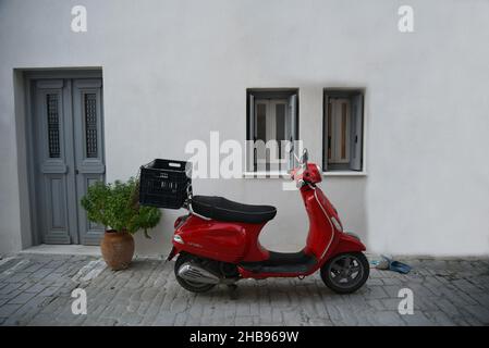 Façade traditionnelle de maison rurale avec un mur blanc, porte et fenêtres en bois gris et un Vespa rouge rétro au premier plan à Koroni, Messinia Grèce. Banque D'Images