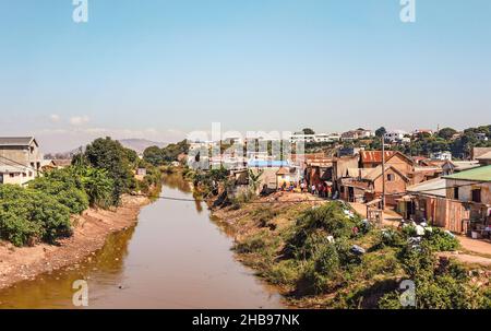 Antananarivo, Madagascar - 07 mai 2019: Le soleil brille sur des maisons simples près de la petite rivière boueuse, peu de gens malgaches marchant, paysage typique de la banlieue Banque D'Images