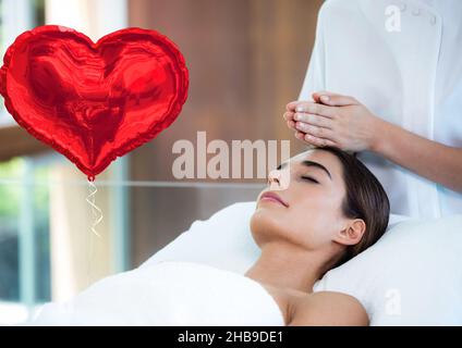 Image composite d'un ballon en forme de coeur rouge contre une femme qui reçoit un massage de la tête dans un spa Banque D'Images