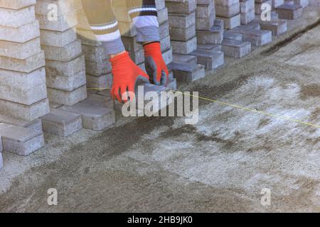 Ouvrier de finisseur d'aménagement paysager posant des pavés sur du sable pour les travaux d'installation de trottoirs Banque D'Images