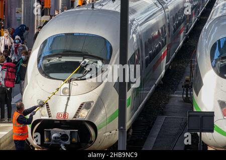 Deux trains longue distance sont à la gare de Munich.Un homme nettoie le pare-brise d'un train DE GLACE.Sur la plateforme, les voyageurs portent des masques Covid Corona. Banque D'Images