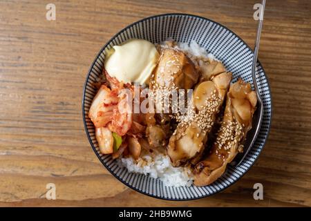 Vue de dessus du bol de riz au poulet grillé Teriyaki avec Kimchi et mayonnaise, sur une table en bois. Banque D'Images