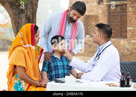 Un médecin indien examine un petit garçon malade au village, une femme portant sari avec son mari et son fils consultant personne médicale,Rural India Healthcare Banque D'Images