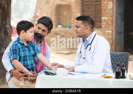 Un docteur indien examine un petit garçon malade au village, le père avec son fils consultant personne médicale, le concept de camp de soins de santé de l'Inde rurale. Banque D'Images