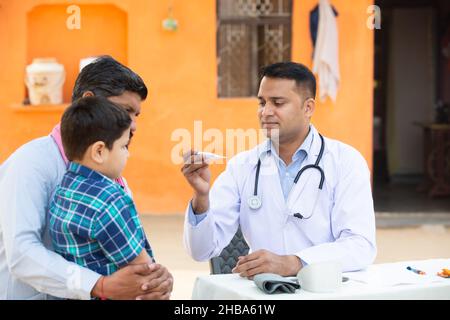 Indian Doctor examine la fièvre du patient de petit garçon de garçon au village avec thermomètre numérique, Père avec son fils consultant personne médicale,Rural Inde guérir Banque D'Images