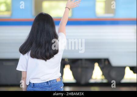 Une adolescente agitant Au revoir à son ami sur un train à pied, une longue femme noire aux cheveux portant un T-shirt blanc debout sur une plate-forme, prise de b Banque D'Images