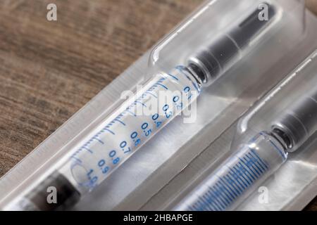 Un portrait en gros plan d'un emballage contenant deux seringues sur une table en bois.Les doses de médicament sont faites d'un tube en verre avec des marques de volume sur lui Banque D'Images