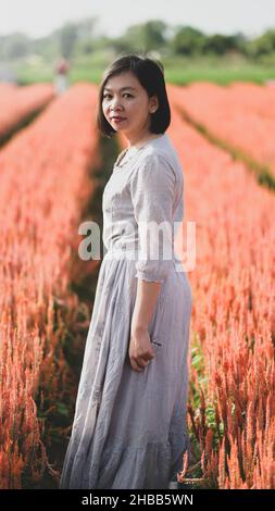 Femme asiatique se promener et prendre des photos dans le jardin de fleurs, elle regarde l'appareil photo et sourit, photo verticale. Banque D'Images