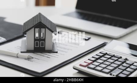 Stylo et maison modèle placés sur des documents contractuels avec calculatrice et ordinateur portable, concept de signature de contrat de construction de maison. Banque D'Images