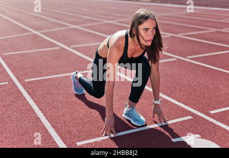 Jeune femme motivée coureur de vêtements de sport prêt à courir sprint à bas démarrage en extérieur Banque D'Images