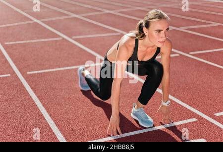 Jeune femme motivée coureur de vêtements de sport prêt à courir sprint à bas démarrage en extérieur Banque D'Images