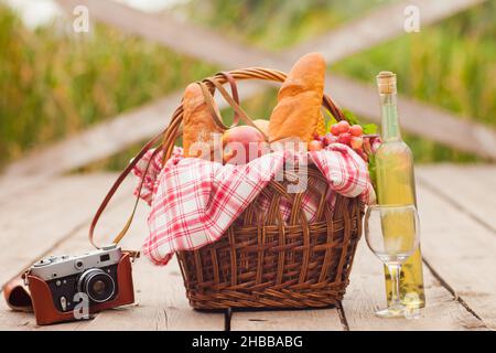 Pique-nique provincial français.Panier pique-nique de style rétro avec nourriture, appareil photo rétro, une bouteille de vin sur la jetée en bois au lac Banque D'Images