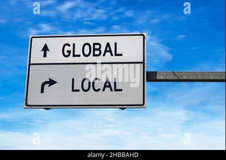 Signalisation routière avec les mots global et local.Deux panneaux de signalisation blancs avec flèche sur poteau métallique sur fond bleu ciel. Banque D'Images