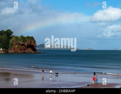 Un arc-en-ciel au-dessus de Tor Bay tandis que les gens s'apprécient sur la plage nord de Goodrington Sands, Paignton, Torbay, South Devon, sud-ouest de l'Angleterre, Banque D'Images