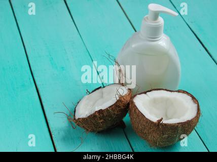 Deux moitiés de noix de coco hachée et une bouteille de crème blanche sur fond de bois bleu.Concept de mode créatif Banque D'Images