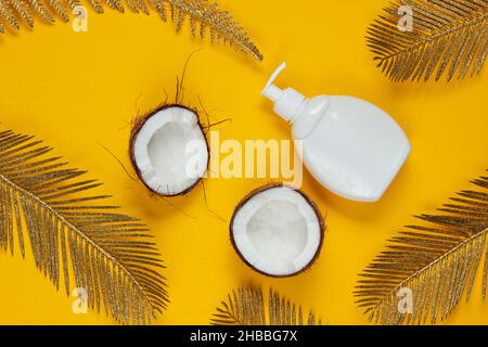 La beauté minimaliste encore la vie.Deux moitiés de noix de coco hachée et une bouteille de crème blanche avec des feuilles de palmier dorées sur fond jaune.Mode créatif Banque D'Images