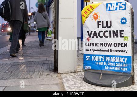 Les acheteurs de Noël marchent au-delà de l'affiche vaccin contre la grippe offrant gratuitement la grippe jab aux personnes admissibles à la pharmacie Sidcup Londres Angleterre Banque D'Images