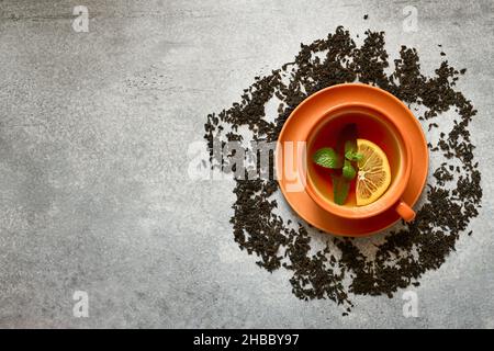 Tasse de thé en céramique orange avec feuille de menthe et tranche de citron sur fond de béton gris avec espace pour copier, vue du dessus Banque D'Images