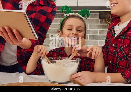 Portrait en gros plan d'un bébé caucasien doux et joyeux souriant sourit un sourire piquant en regardant l'appareil photo assis à une table de cuisine entre son frère A. Banque D'Images